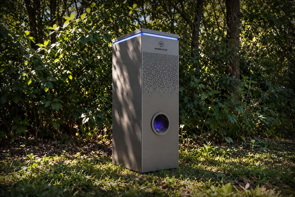 Trampa antimosquitos MOSQUITOR ONE instalada en un jardín con vegetación, con acabado gris antracita y luz LED azul.